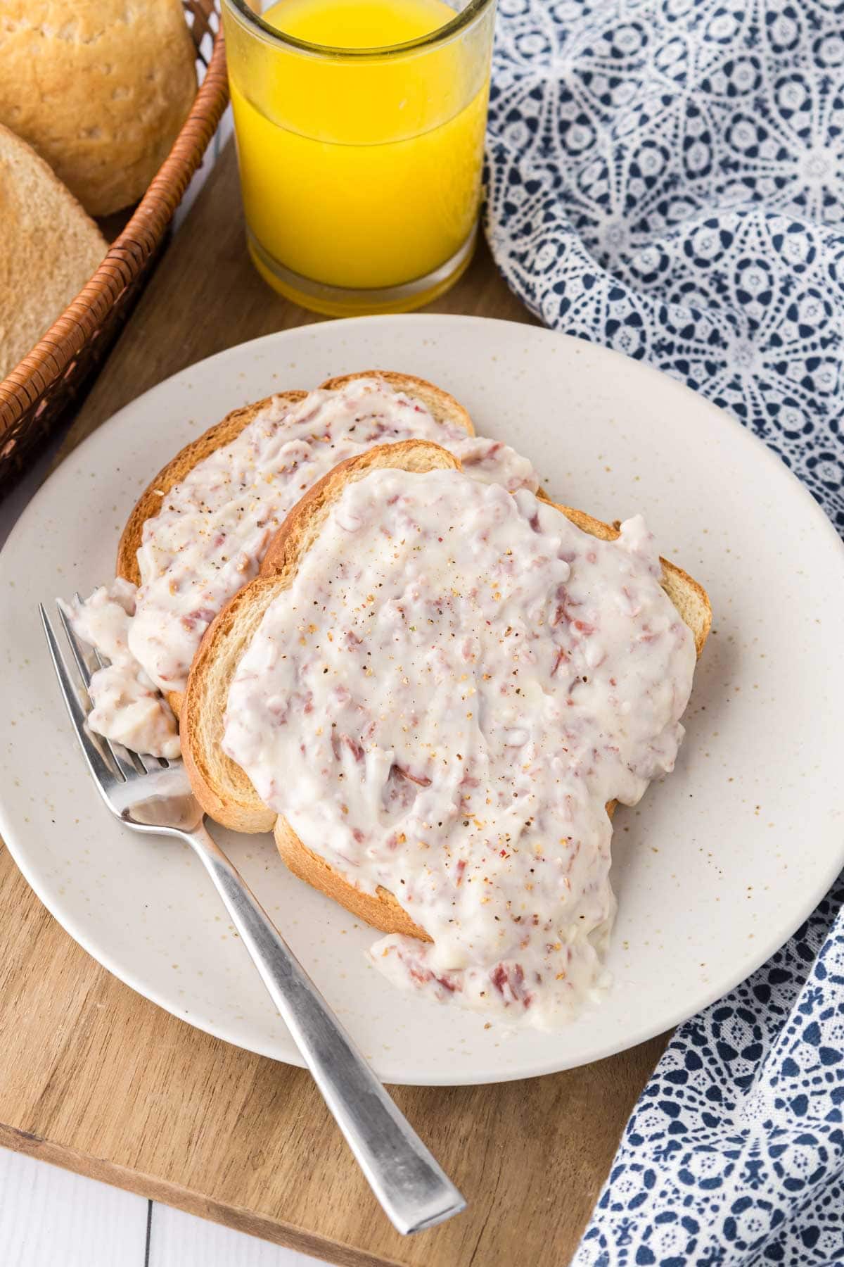 A white plate with two slices of toast covered in creamy chipped beef gravy.