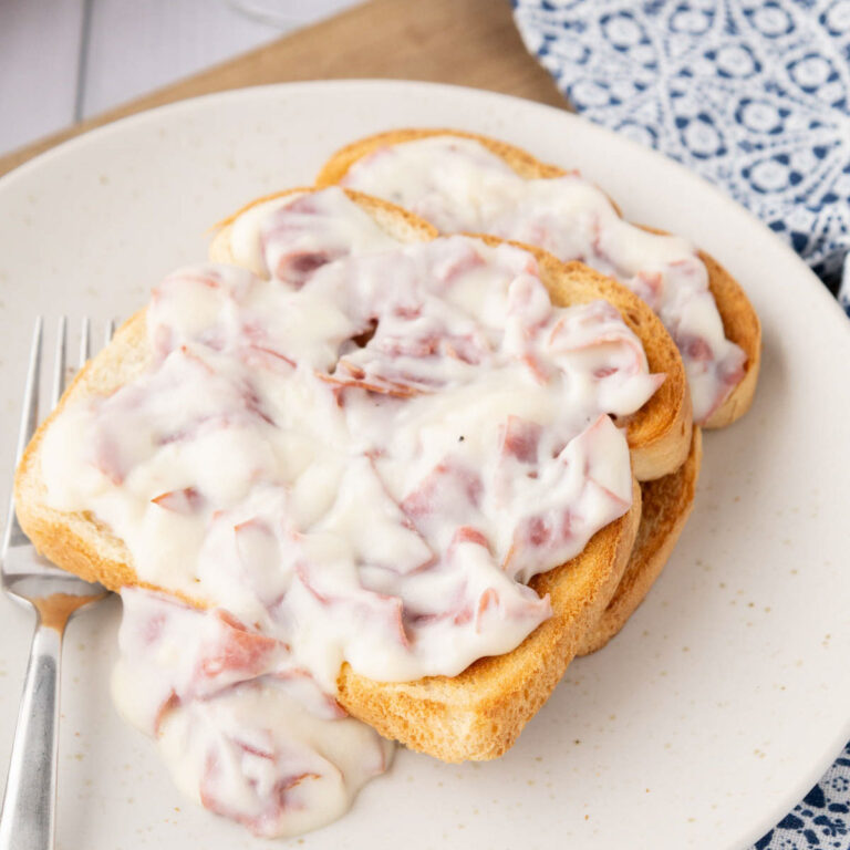 Two slices of toast on a plate with creamed chip beef gravy on top and sprinkled with black pepper.