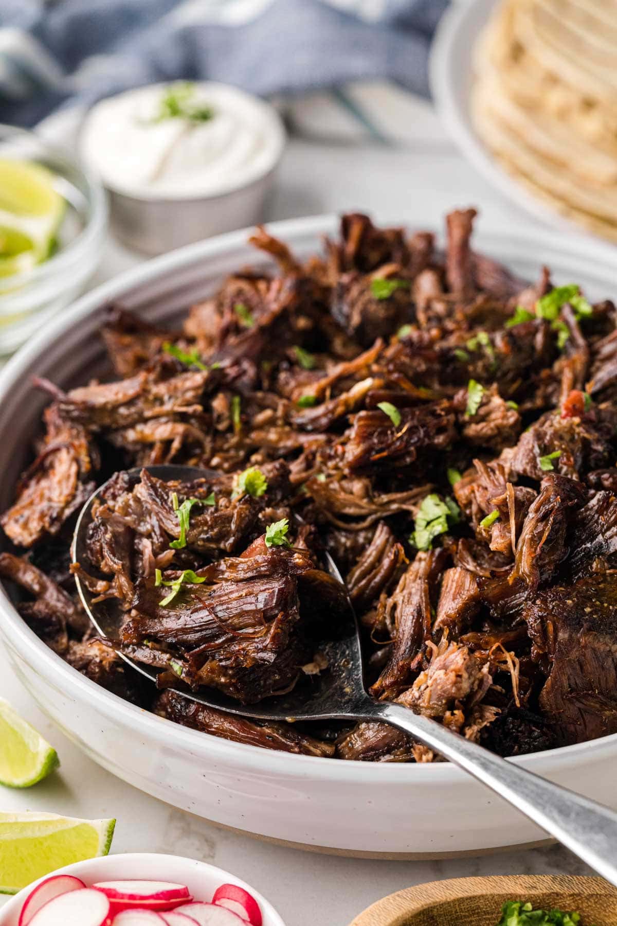 A white bowl filled with tender beef with a silver scoop removing a scoop.