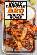 Honey Chipotle BBQ wings are featured on a baking tray with dipping sauce and carrots sticks.