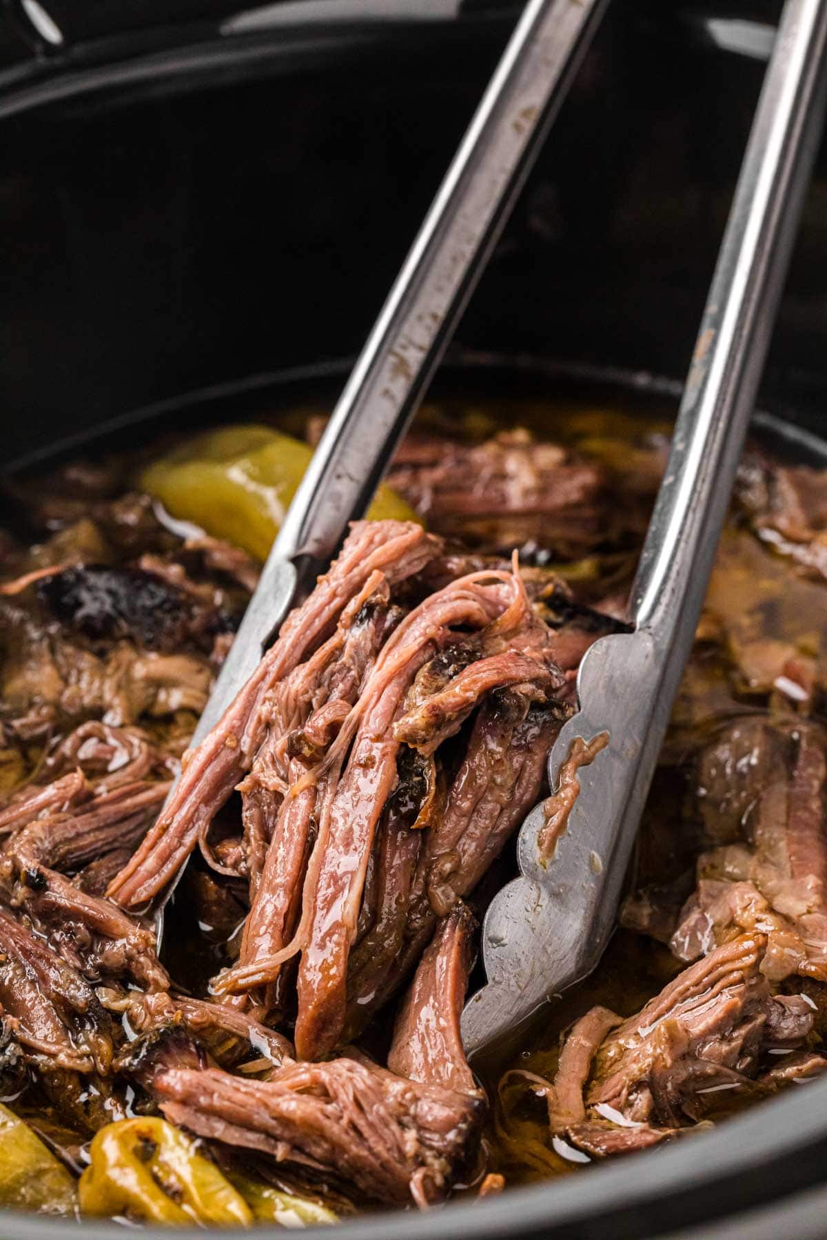 Tongs removing a serving of tender Mississippi beef roast from the slow cooker.