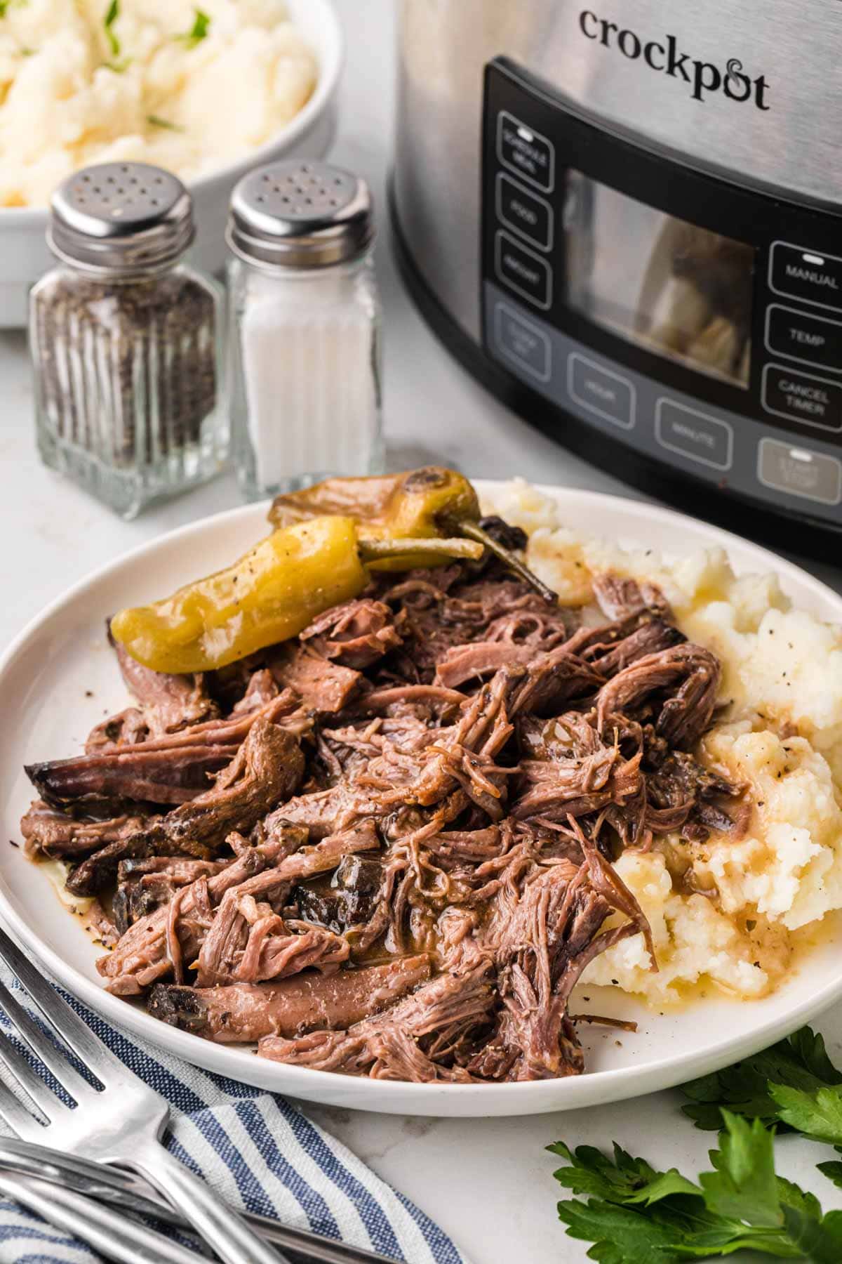 A white plate with a bed of creamy mashed potatoes topped with shredded Mississippi pot roast.