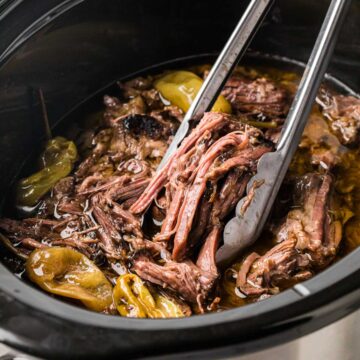 Tongs removing a serving of tender Mississippi beef roast from the slow cooker.