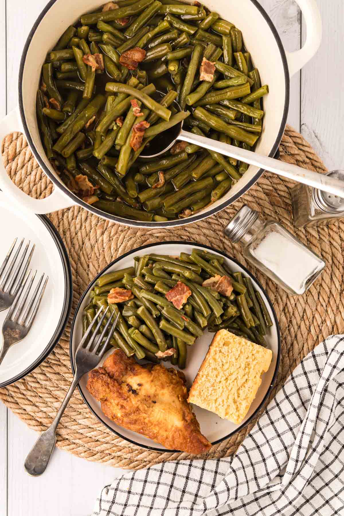 A tablescape a pot of green beans with a southern style plate of green beans, cornbread, and fried chicken.