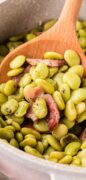 A closeup image of the Baby lima beans is showing the beans and bacon on a wooden serving spoon.