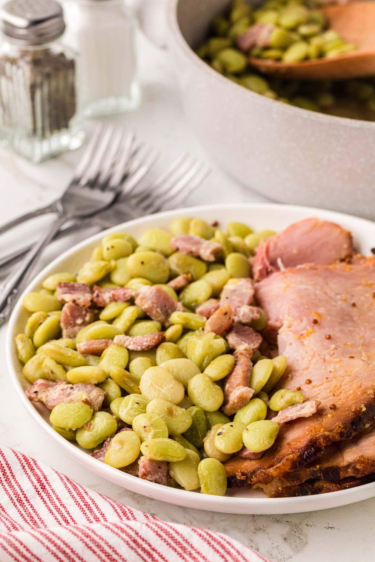 Lava beans on a white plate with sliced ham.