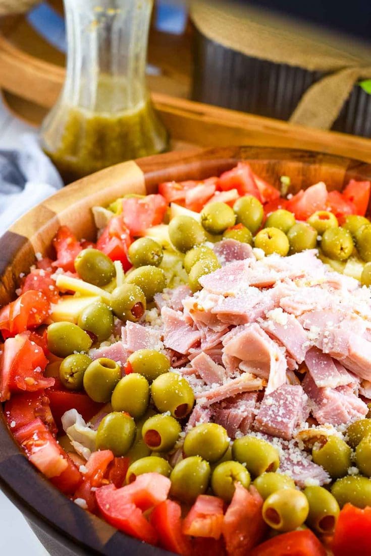A large wooden serving bowl of this Columbia Restaurant\'s 1905 salad recipe topped with ham, green olives, and pepperoni 