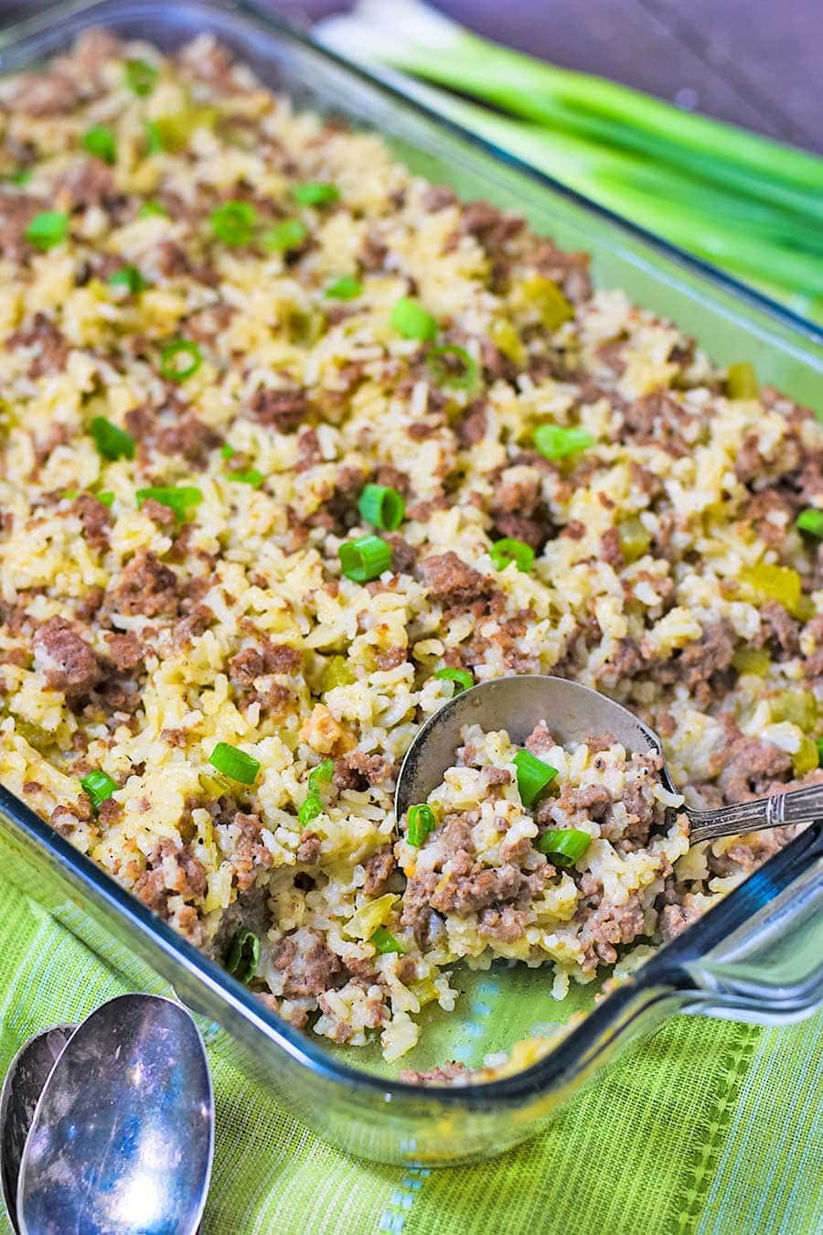 a casserole dish filled with beef and sausage rice casserole and a serving spoon