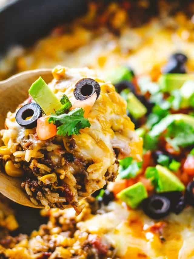 Upclose image of a scoop of ground beef and rice with cheese, avocado, black olives and tomatoes on top.