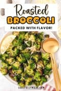 A white serving bowl and gold serving spoon is filled with oven-roasted broccoli and garnished with a lemon wedge.