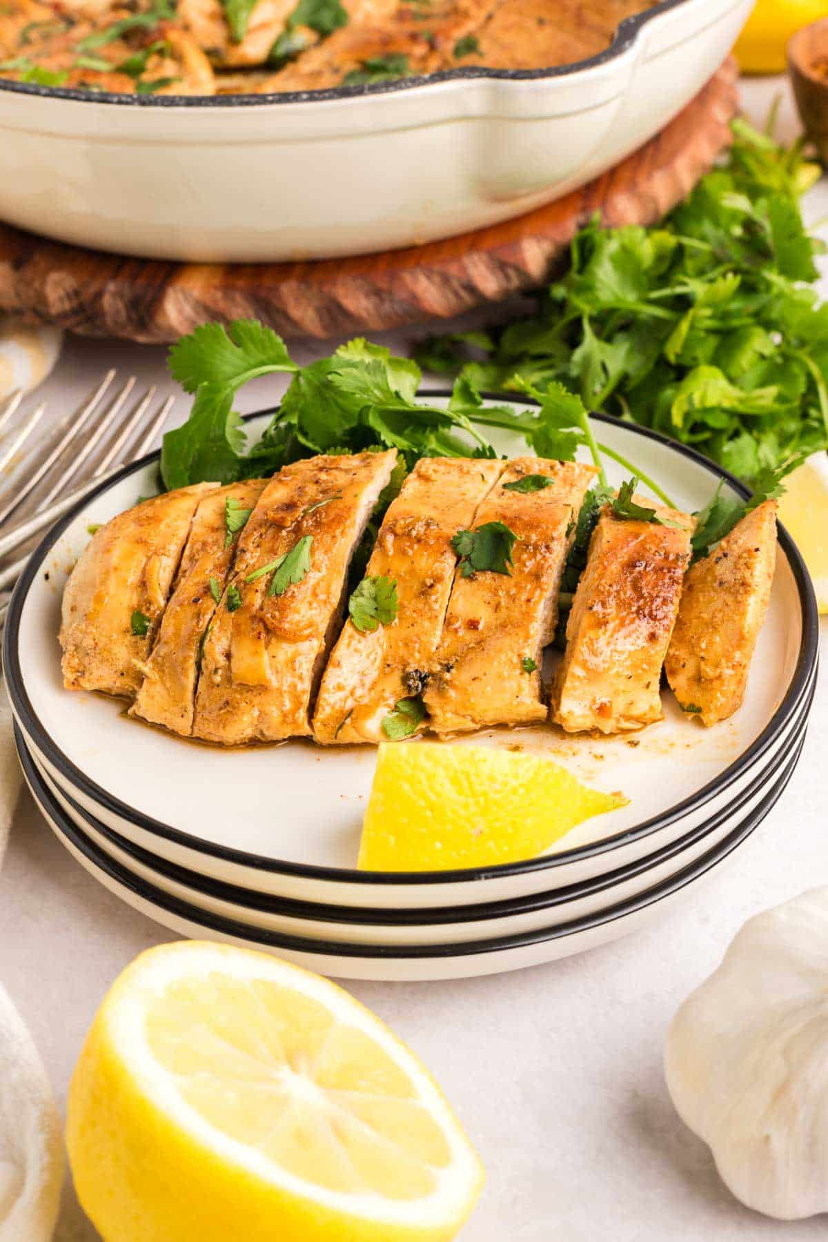 A slice pan fried greek chicken breast on a white plate with a slice of lemon.
