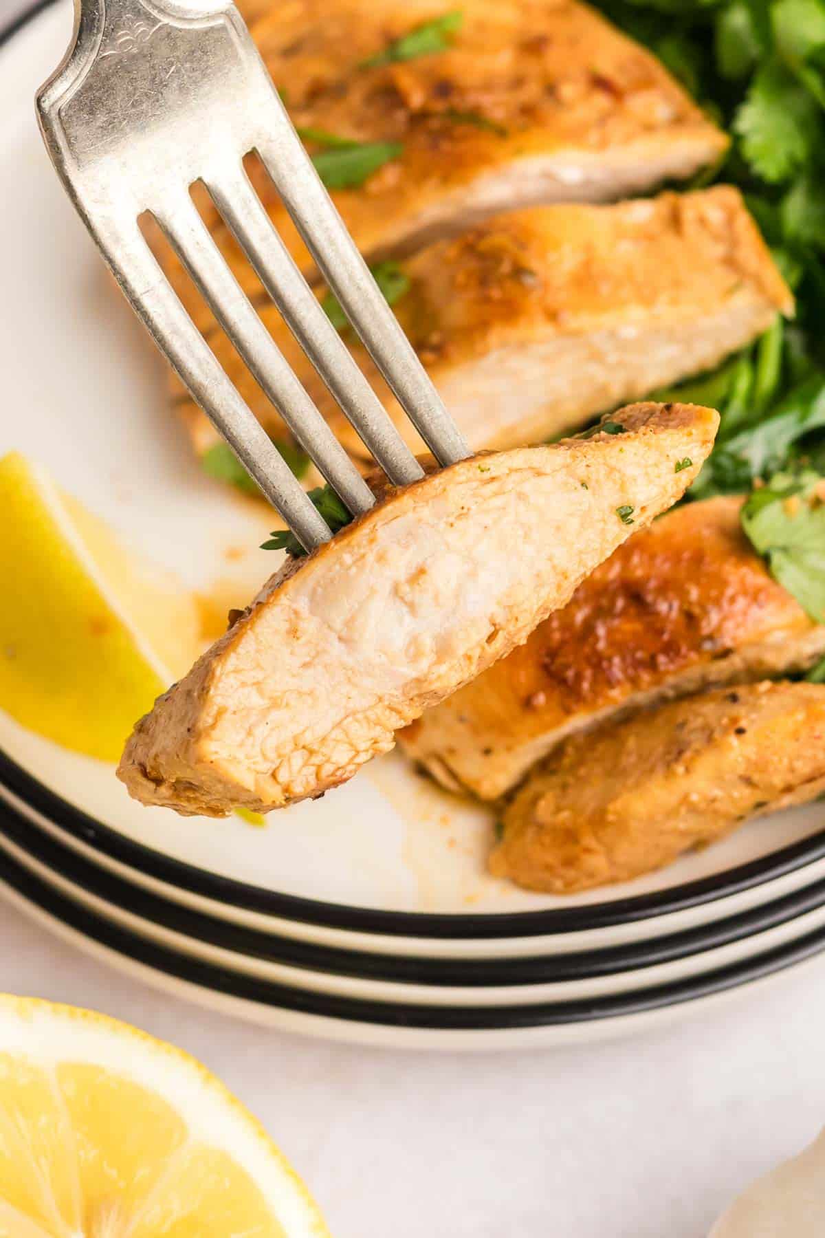 A fork picking up a slice of greek chicken showing the juicy inside of the bite.
