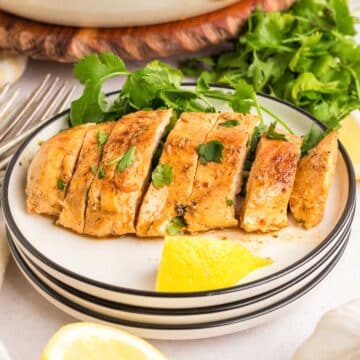 A sliced pan fried greek chicken breast on a white plate with a slice of lemon.