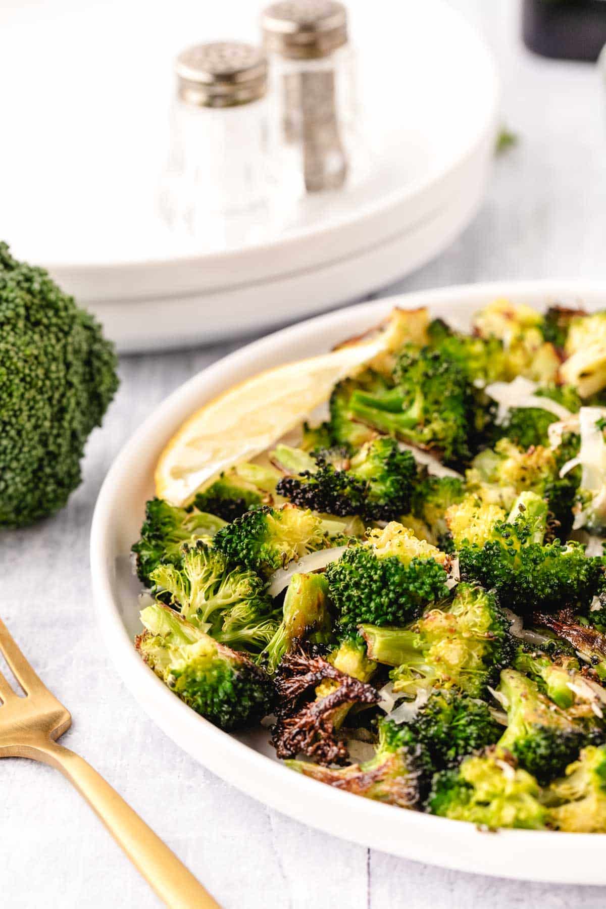 A white dinner plate with roasted broccoli and a wedge of lemon.
