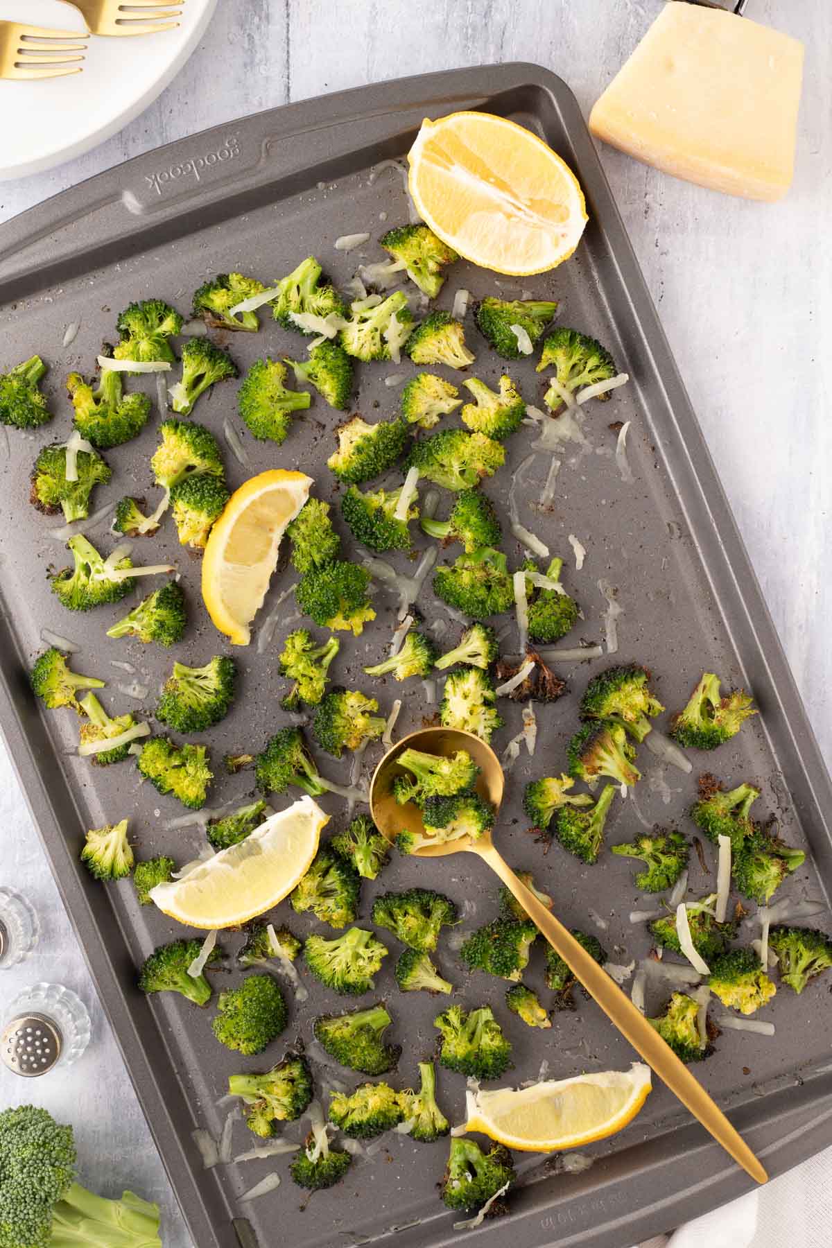 Roasted broccoli being served with a gold serving spoon from the baking sheet.