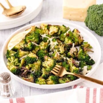 A white dinner plate with roasted broccoli and a wedge of lemon.
