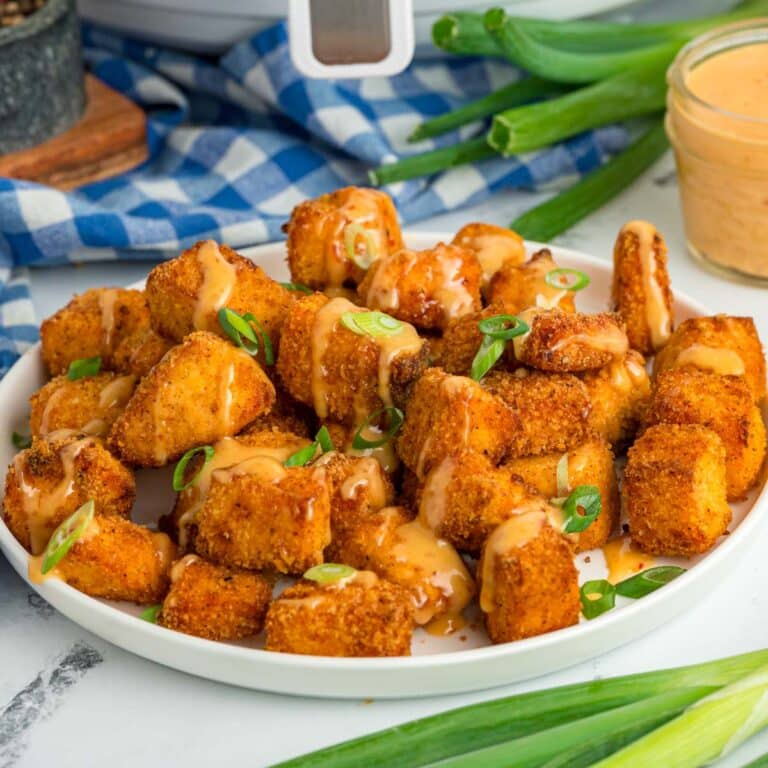 Crispy Salmon Bites on a white plate topped drizzle with bang bang sauce and garnished with sliced green onions.