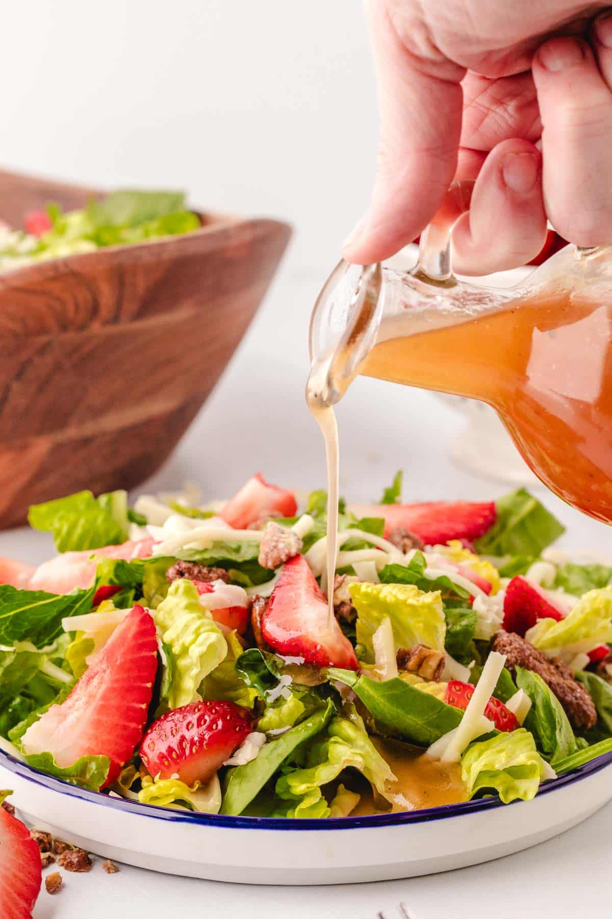 Pouring honey red wine dressing on a strawberry salad.