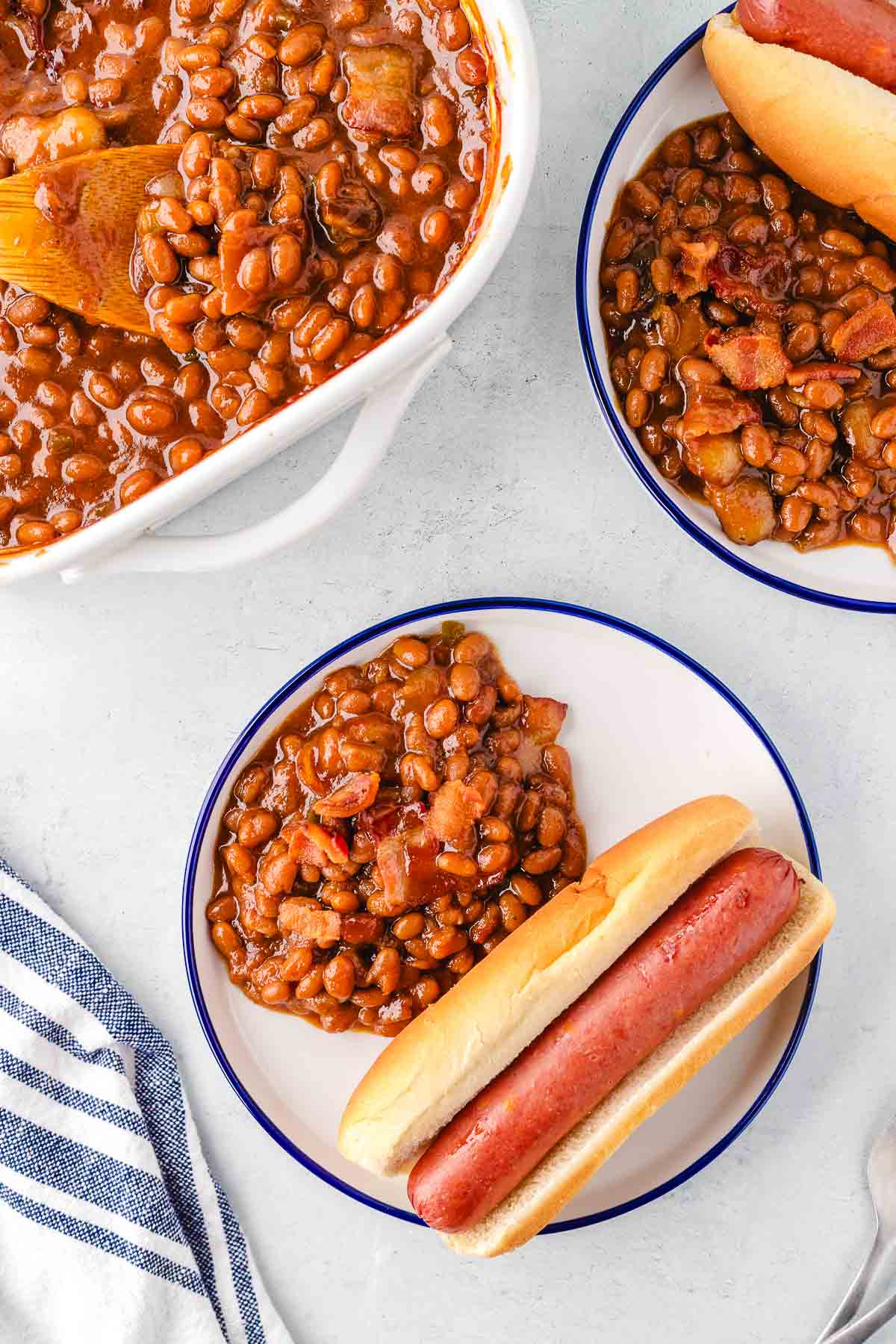 A plate with a hot dog in a bun and a side of baked beans.