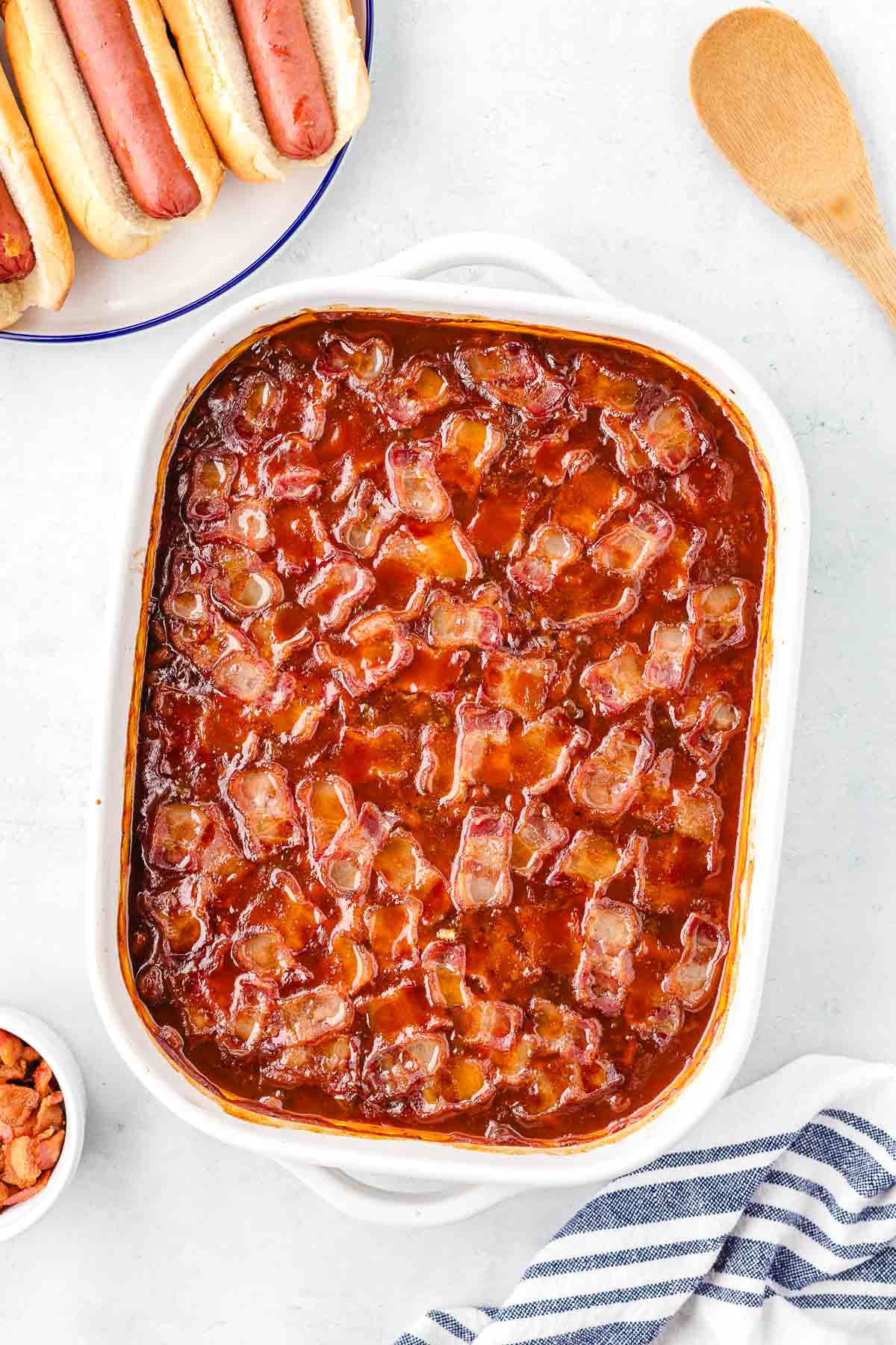 A white casserole dish with oven-baked baked beans topped with crispy bacon.