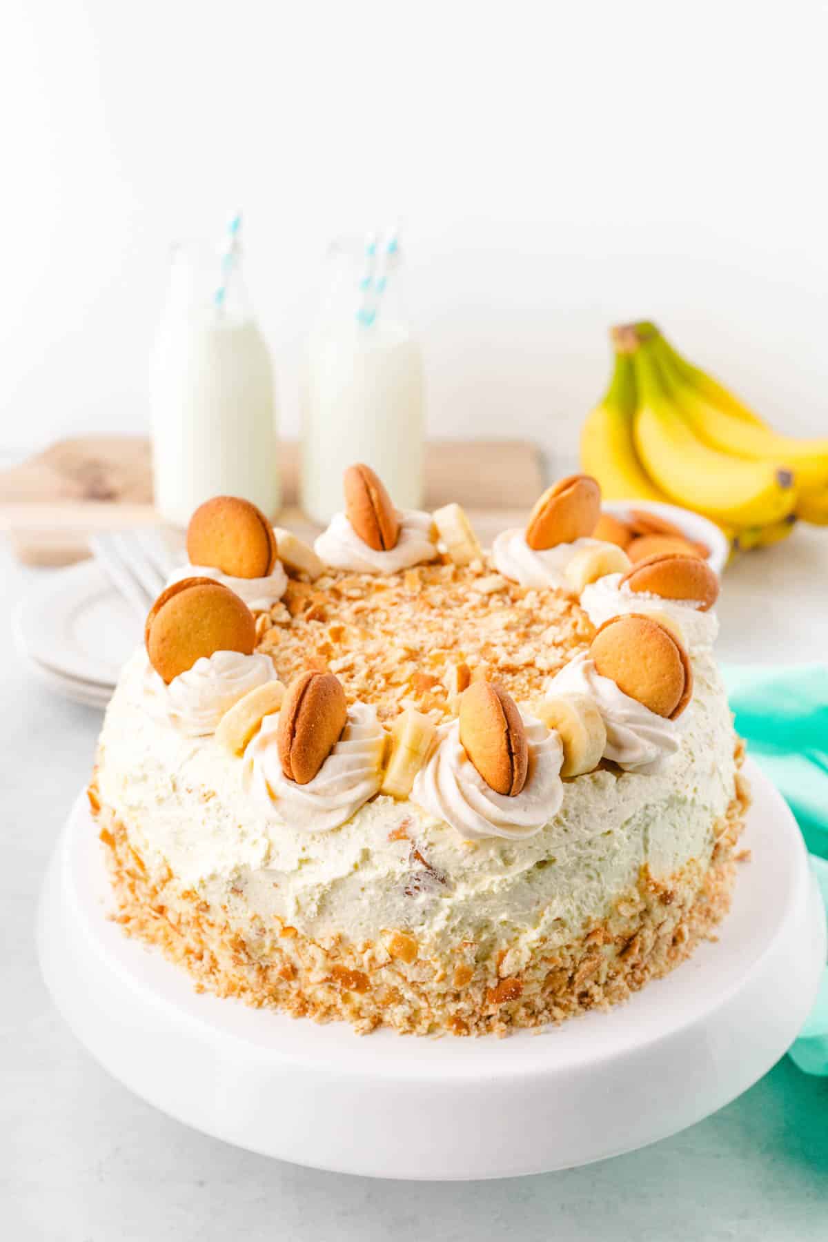 A banana pudding cake garnished with vanilla wafers and slice bananas on a white cake pedestal.