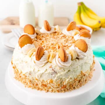 A banana pudding cake garnished with vanilla wafers and slice bananas on a white cake pedestal.