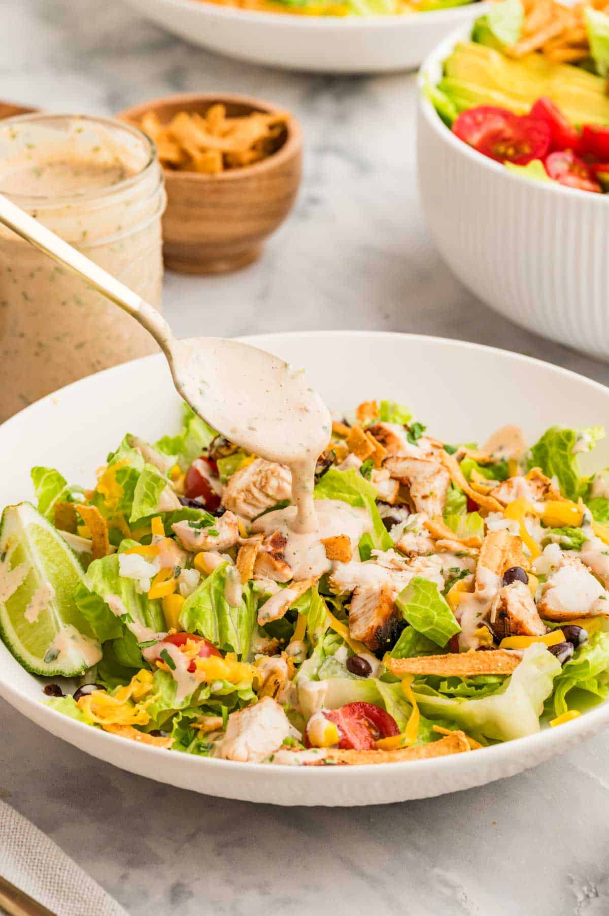 Spooning a creamy bbq lime dressing on top of salad.