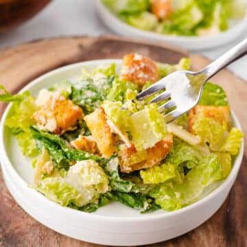A homemade caesar salad on a white plate with a fork removing a bite.