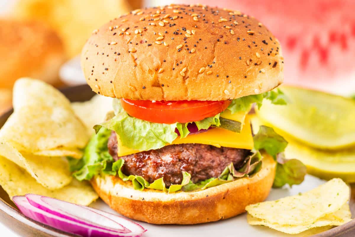 Air fryer hamburger on a sesame seed bun with lettuce, tomato onion, pickles, and served with chips.