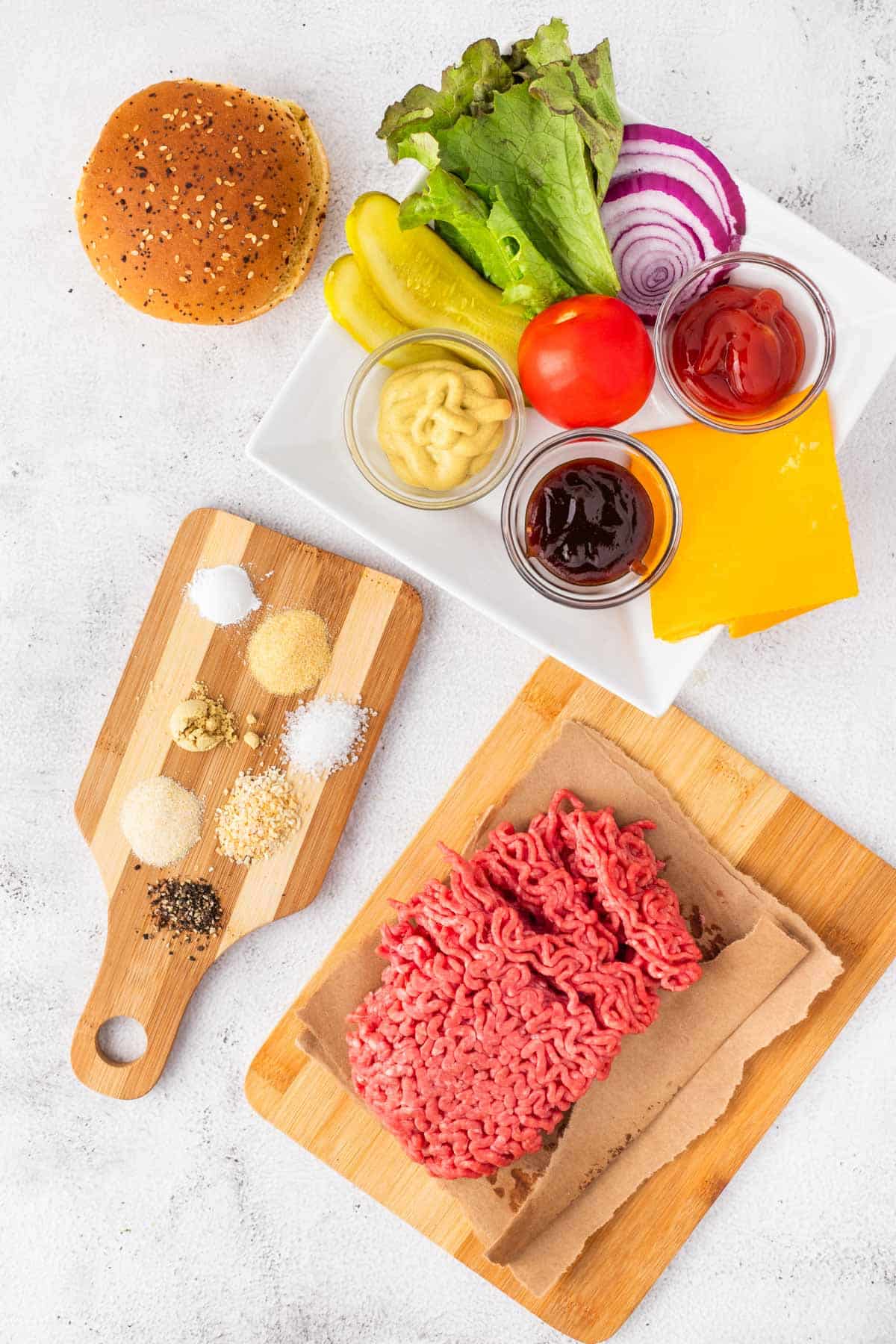 An image of ground beef, seasonings, and burger condiment ingredients.