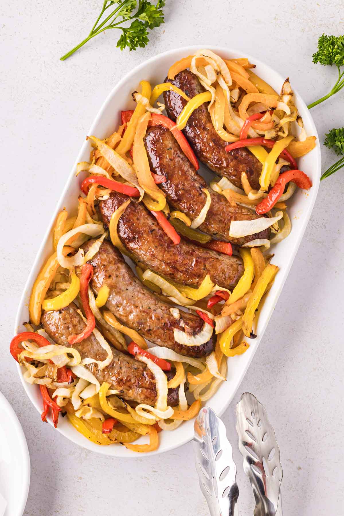 A white serving plate filled with Italian sausage with slice onions and peppers.