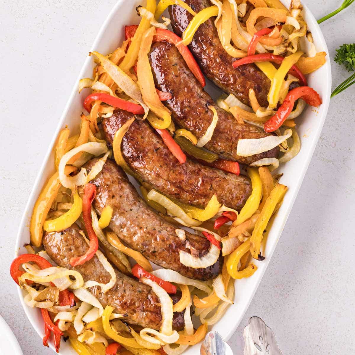 A white serving plate filled with Italian sausage with slice onions and peppers.