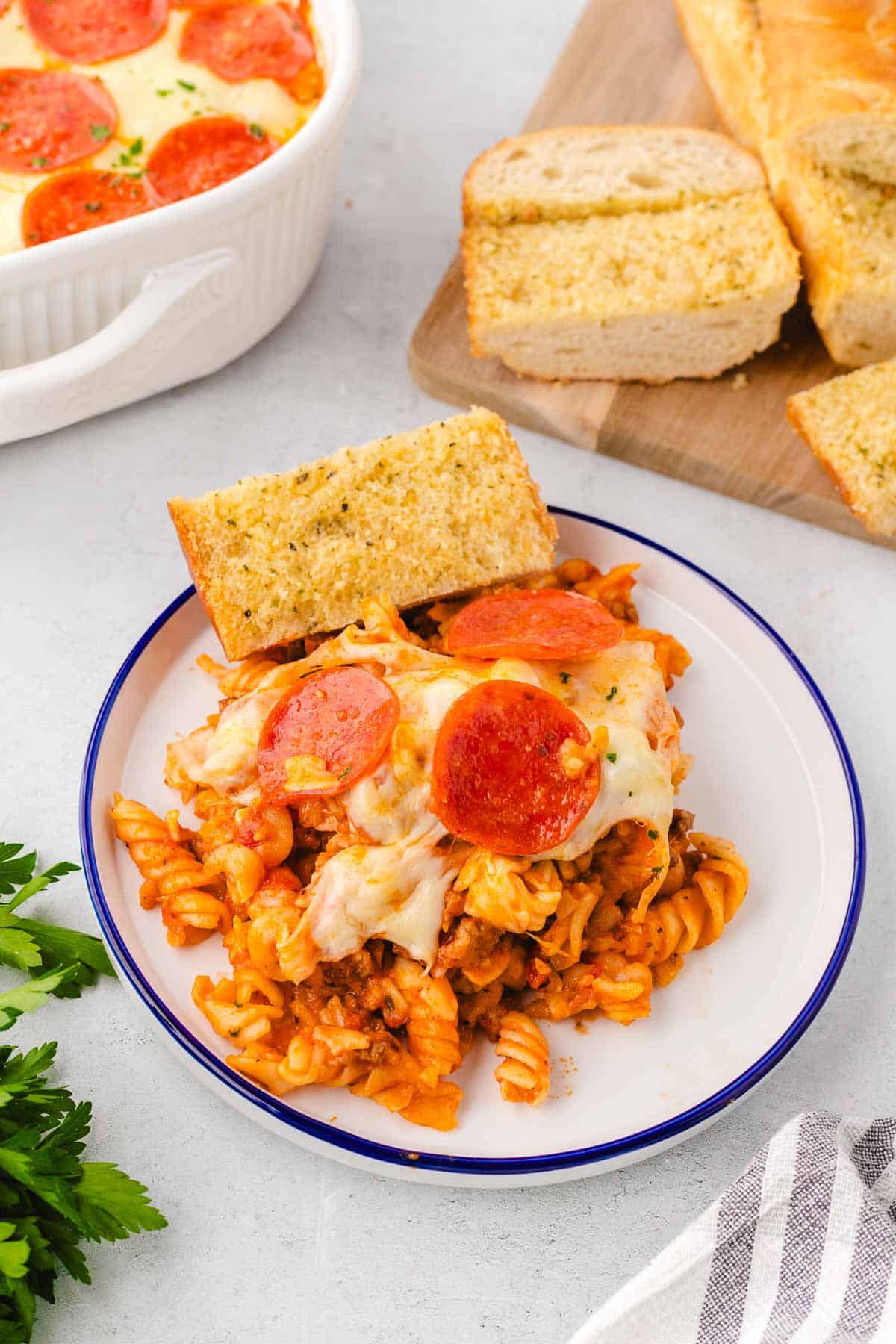 A plate with a serving of pizza pasta bake and a slice of garlic bread.