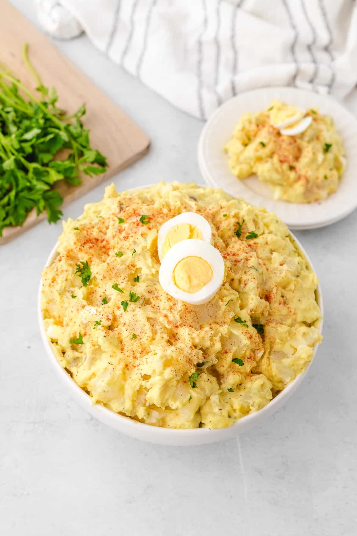 A white bowl filled with southern potato salad garnished with sliced boiled eggs, parsley, and paprika.