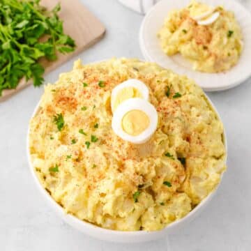 A white bowl filled with southern potato salad garnished with sliced boiled eggs, parsley, and paprika.