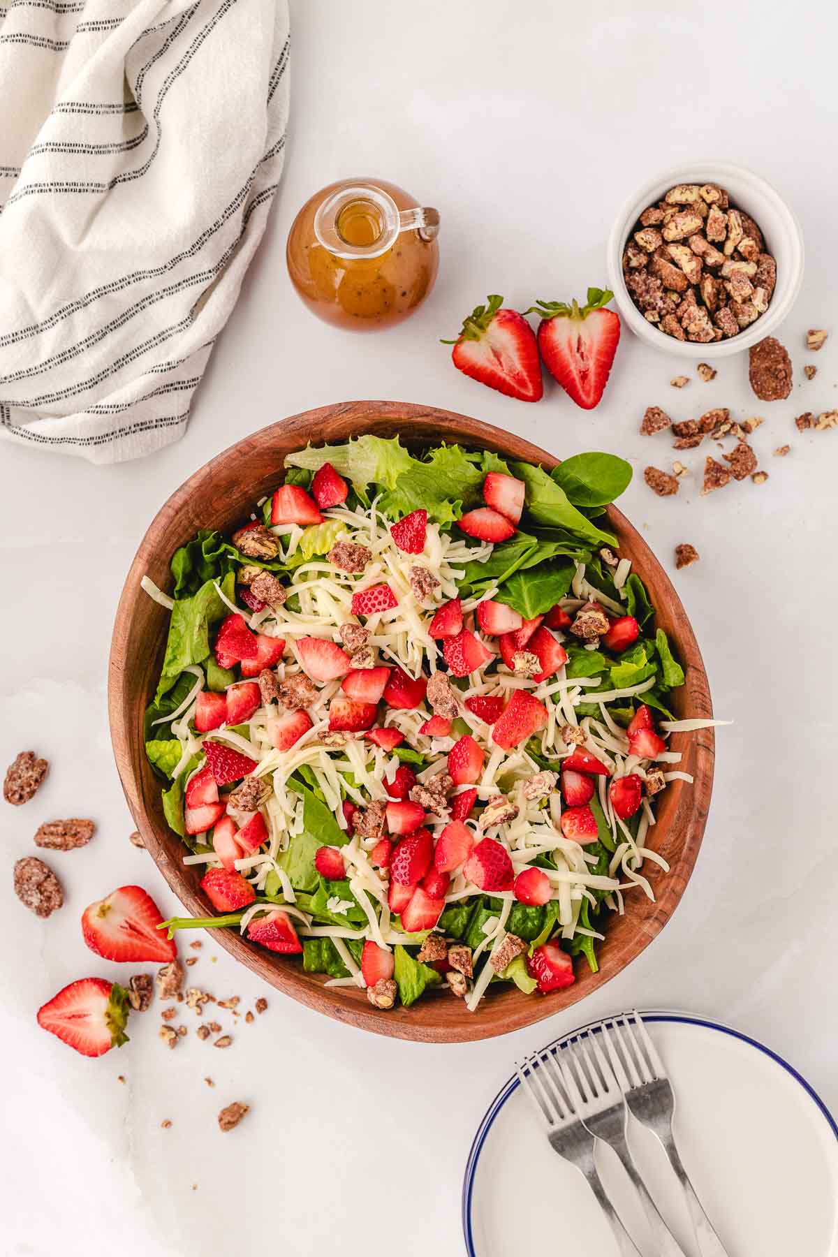 A wooden bowl filled with a summer strawberry salad with candied pecans, mozzarella cheese, greens, and a homemade sweet vinaigrette dressing