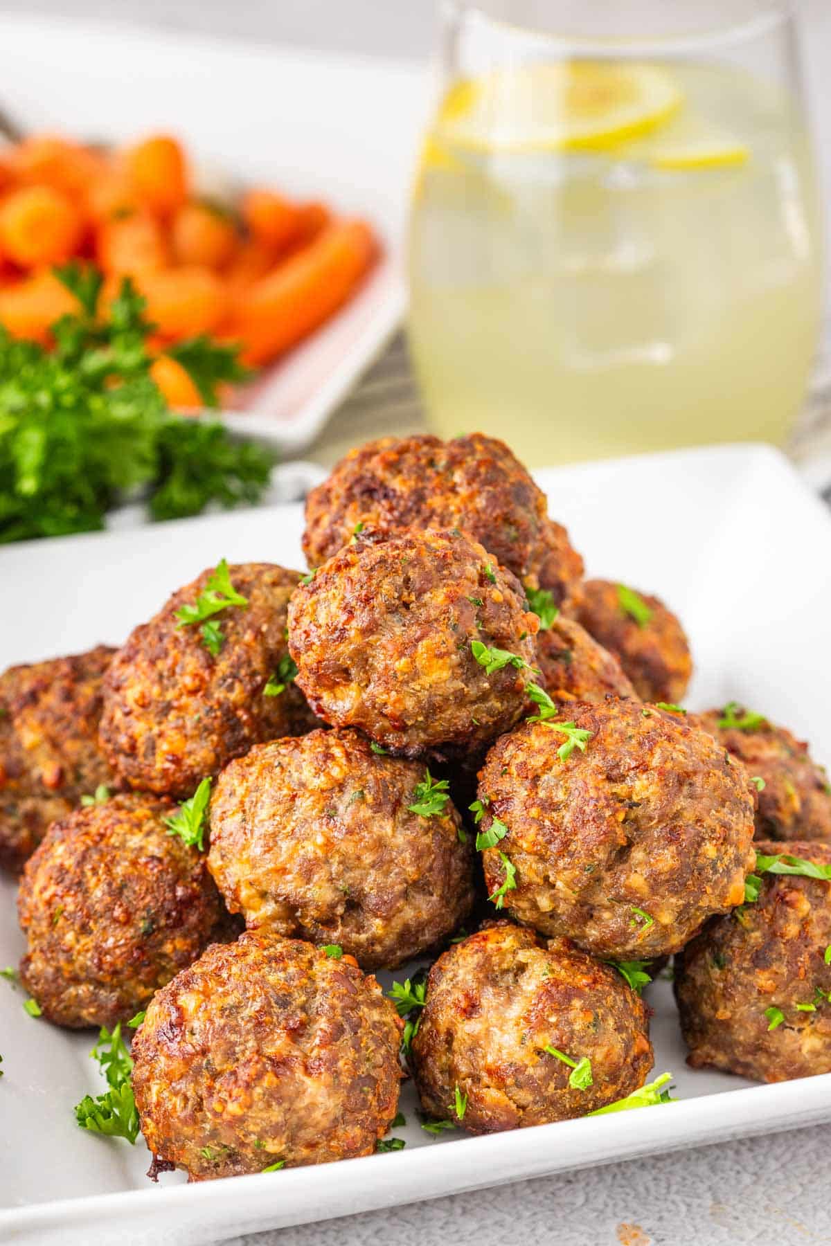 A plate of meatballs, garnished with parsley with a picture of lemonade in the background.