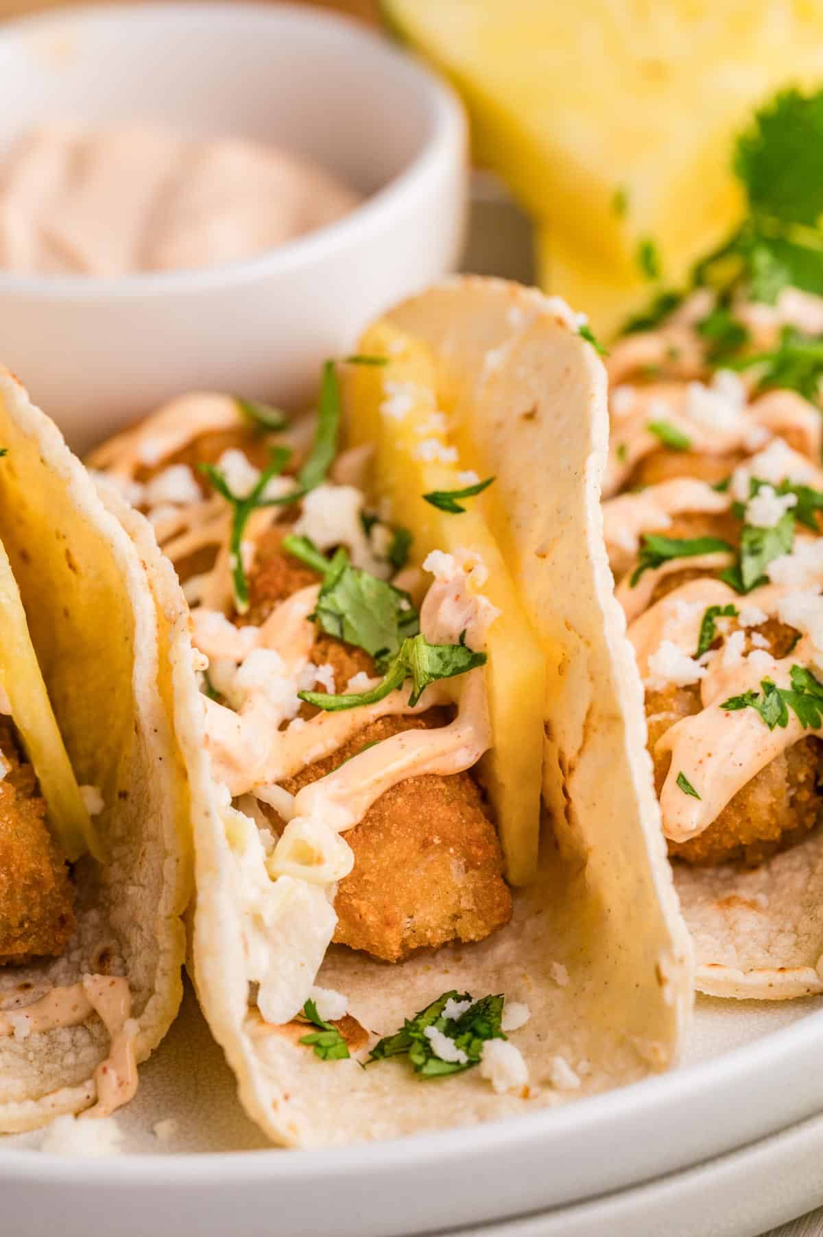 An up close image showing three fish stick tacos, drizzled with Sriracha lime creamer, and garnished with cilantro and Cotija cheese.