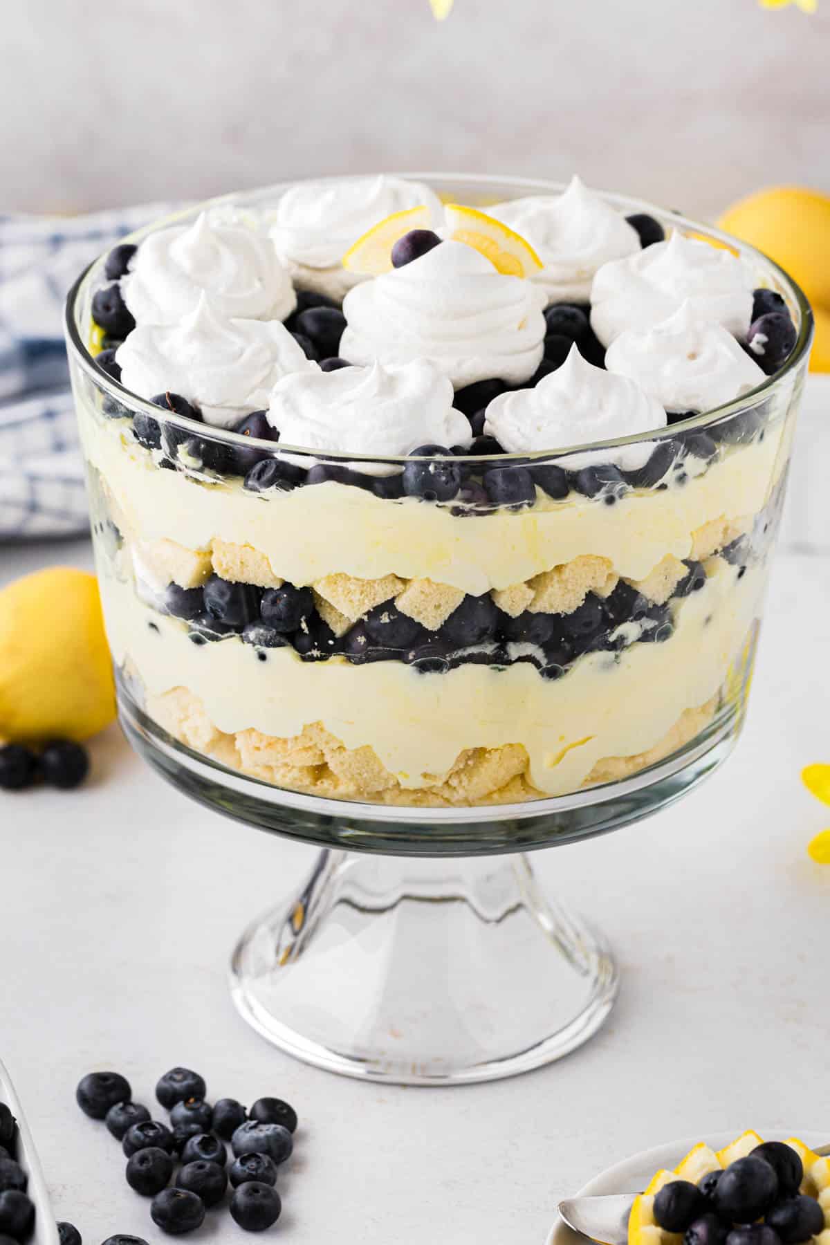 A glass trifle bowl with layers of lemon pudding, blueberries, pound cake and whipped cream.