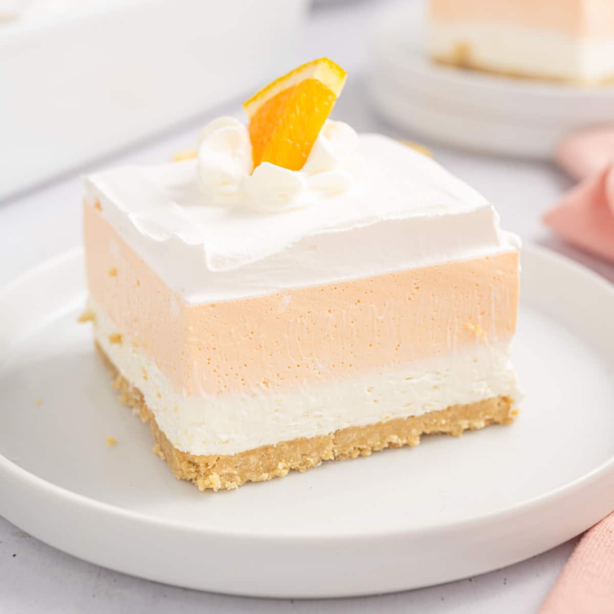 A slice of orange Creamsicle bars on a white plate topped with a slice of orange.