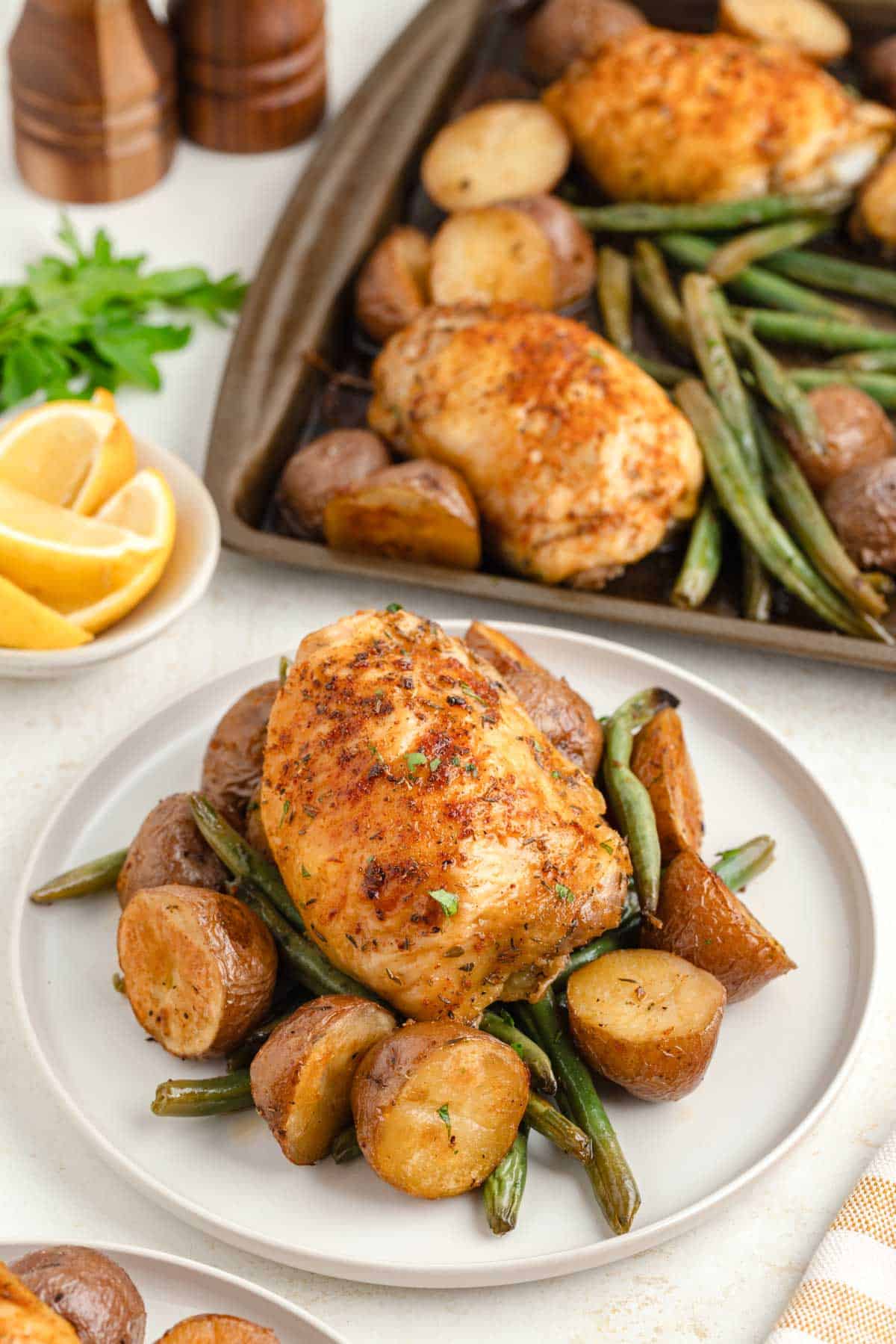 A white plate with sheet pan baked chicken on top of a bed of roasted red potatoes, and green beans.