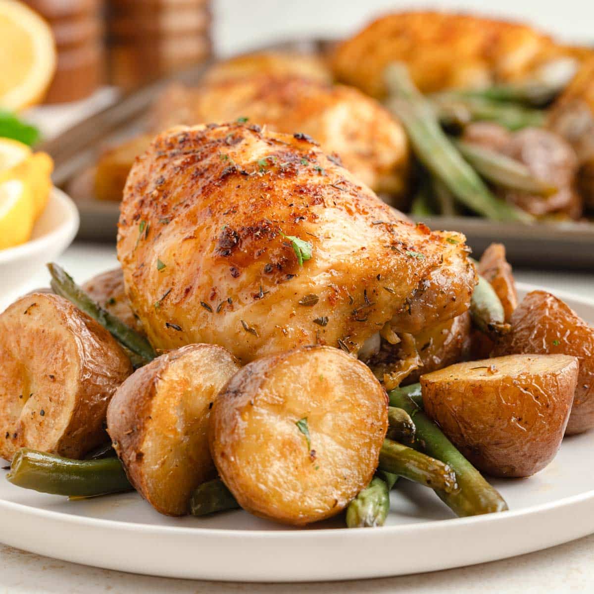 A white plate with sheet pan baked chicken on top of a bed of roasted red potatoes, and green beans.