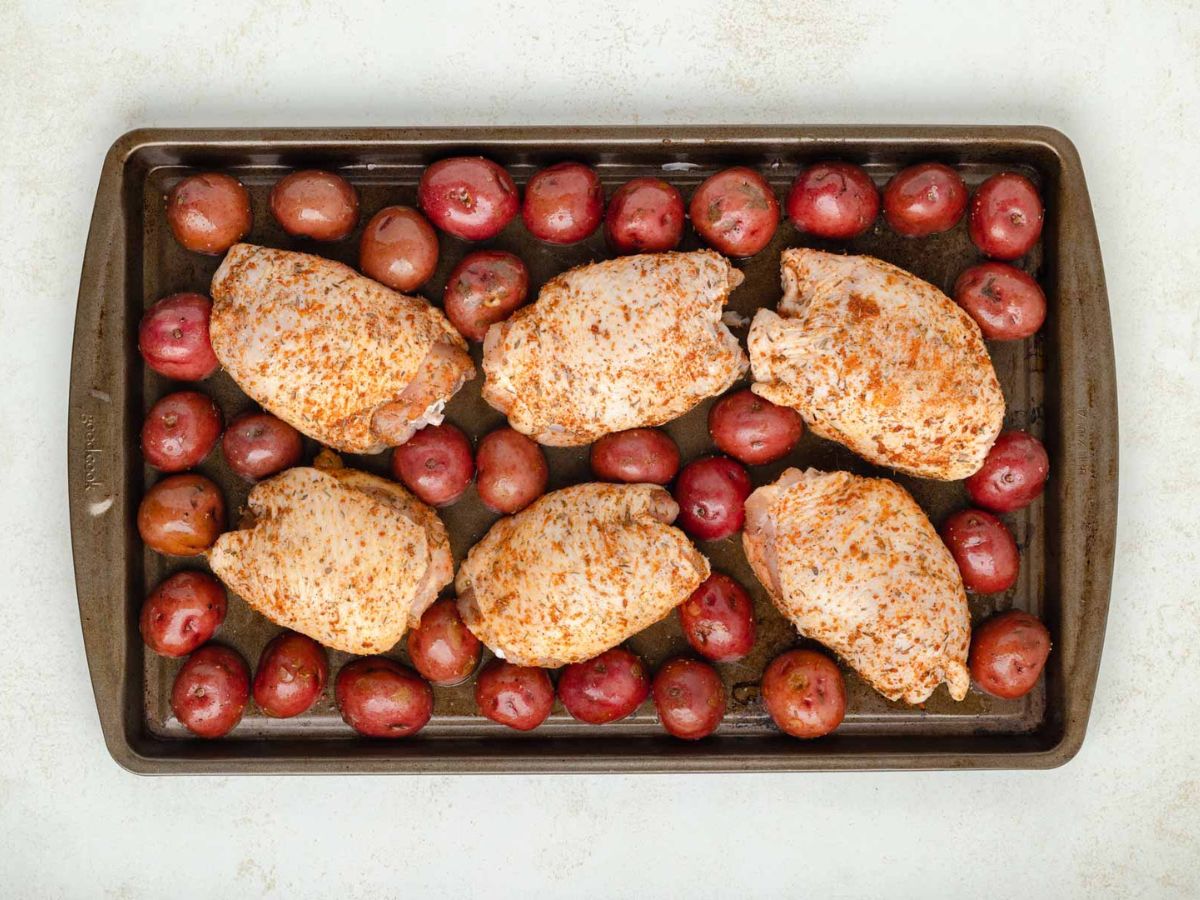 A sheet pan with seasoned chicken thighs and baby red potatoes.