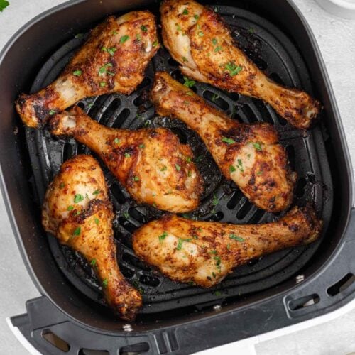 An air fryer basket with perfectly seasoned crispy cooked chicken legs.