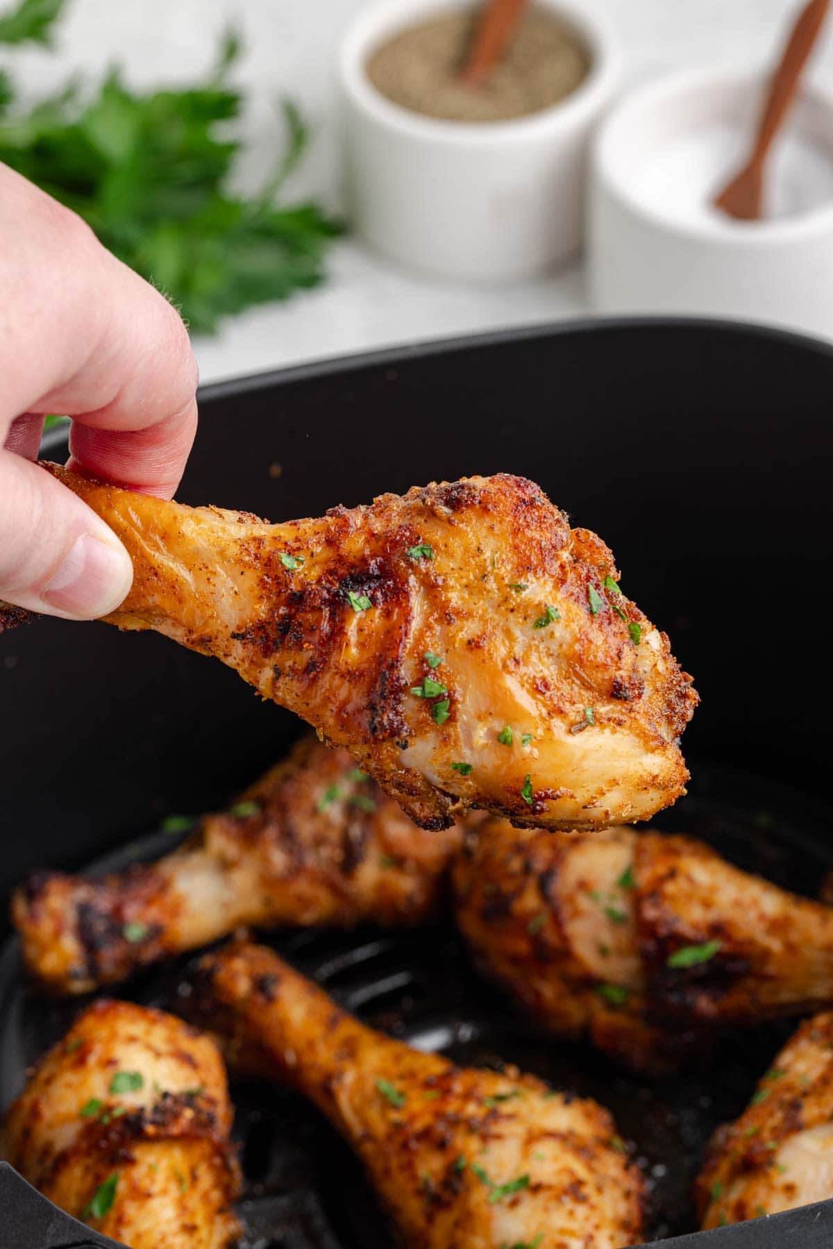 A hand removing a chicken leg from the air fryer basket.