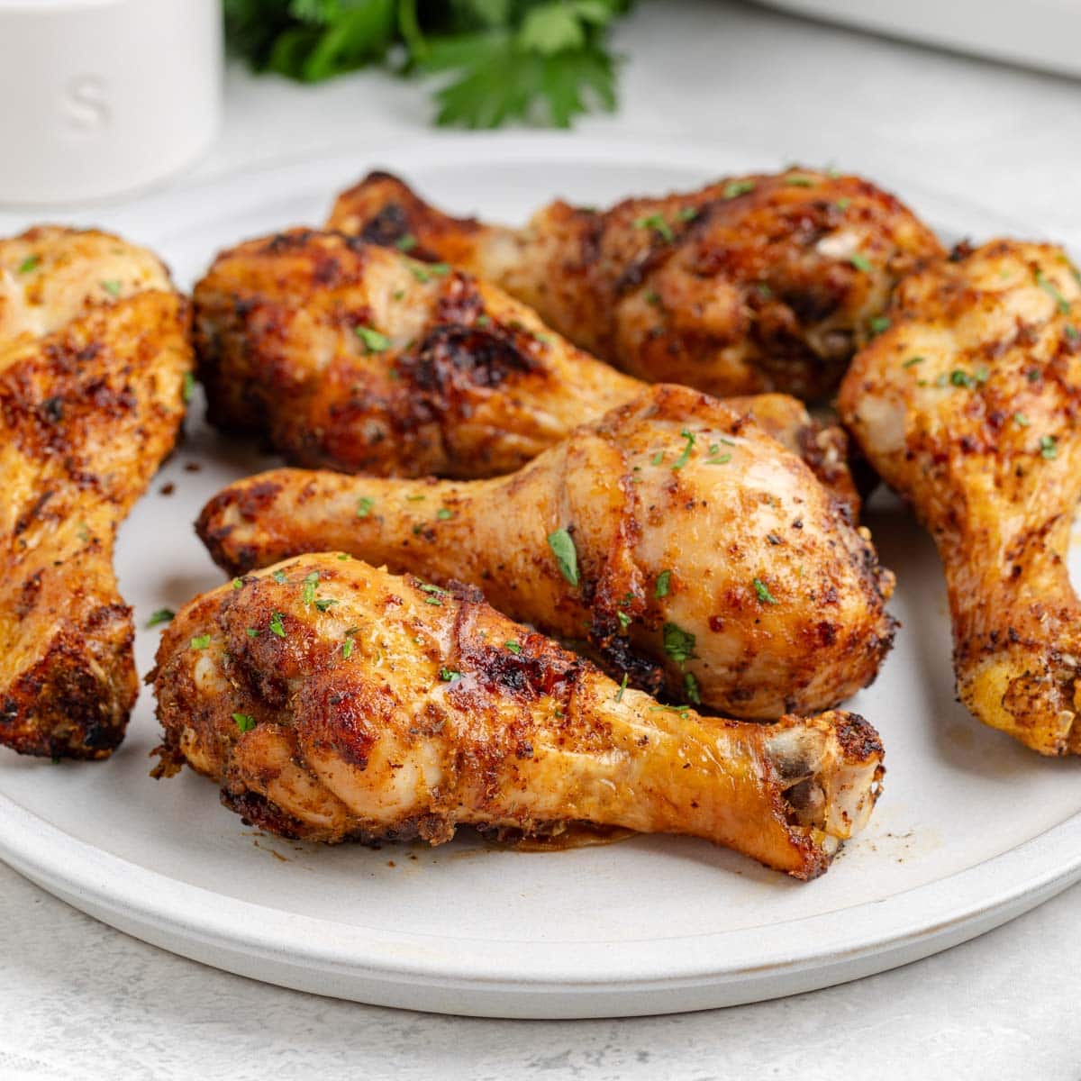 A beige serving plate filled with perfectly crispy air fryer chicken drumsticks.