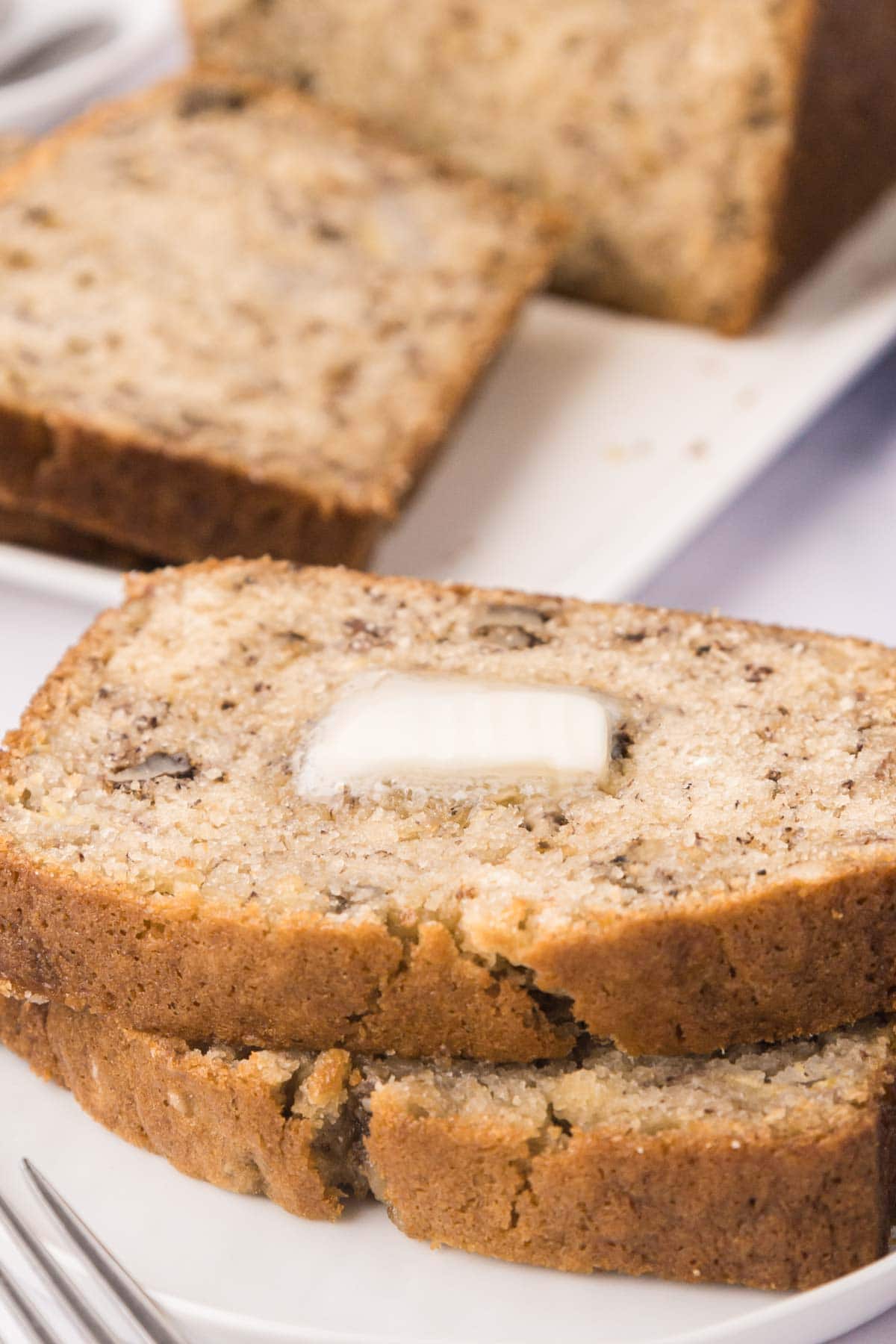 Two slices of banana bread topped with a pot of butter that is melting into the bread.