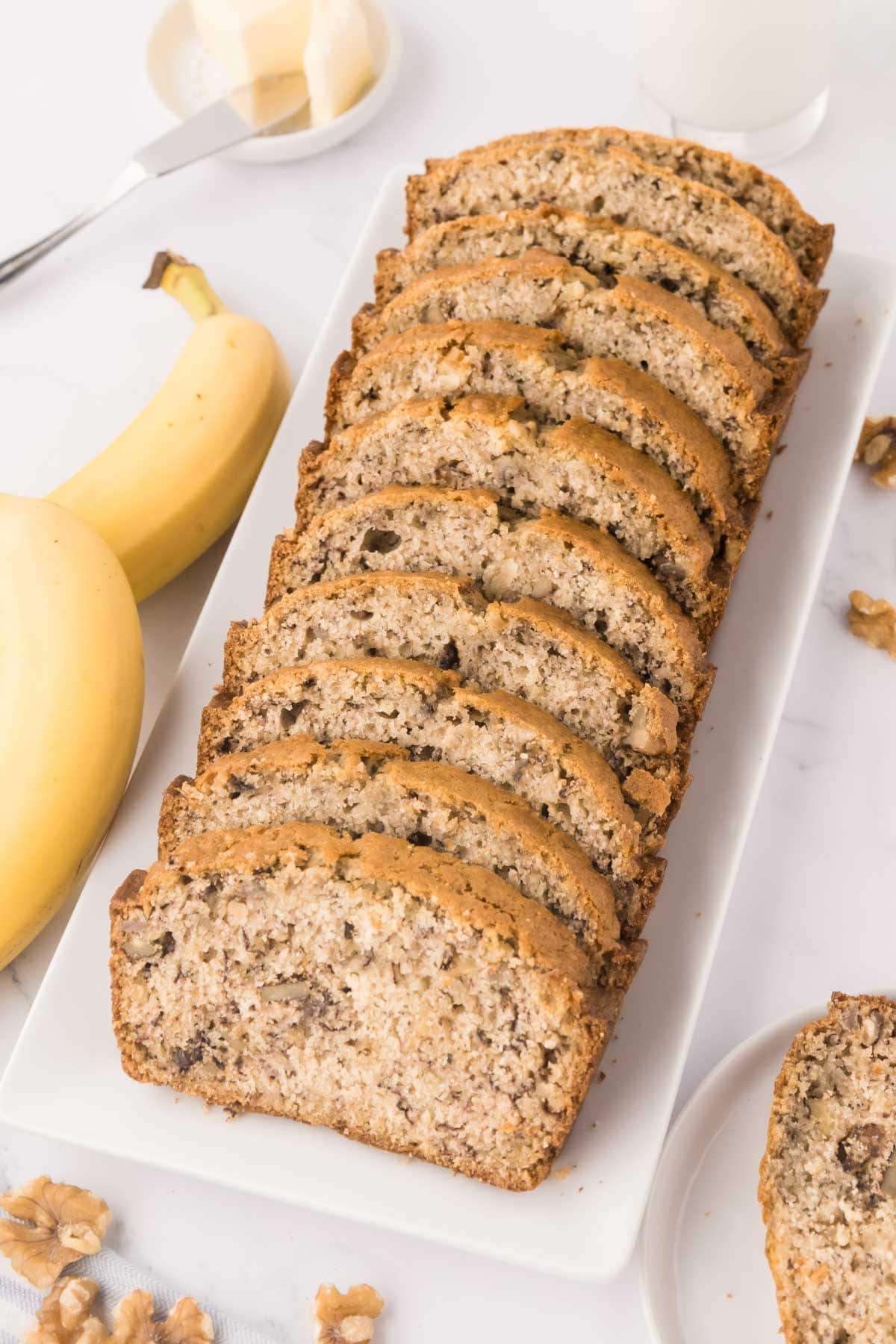 A white serving tray with sliced buttermilk banana bread with walnuts.