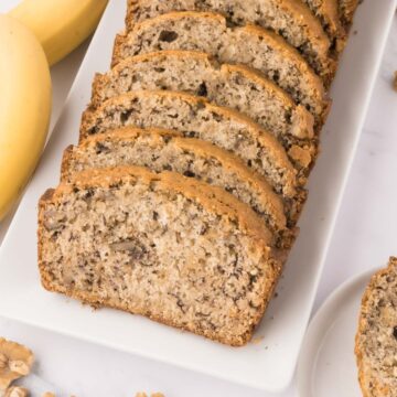 A white serving tray with sliced buttermilk banana bread with walnuts.