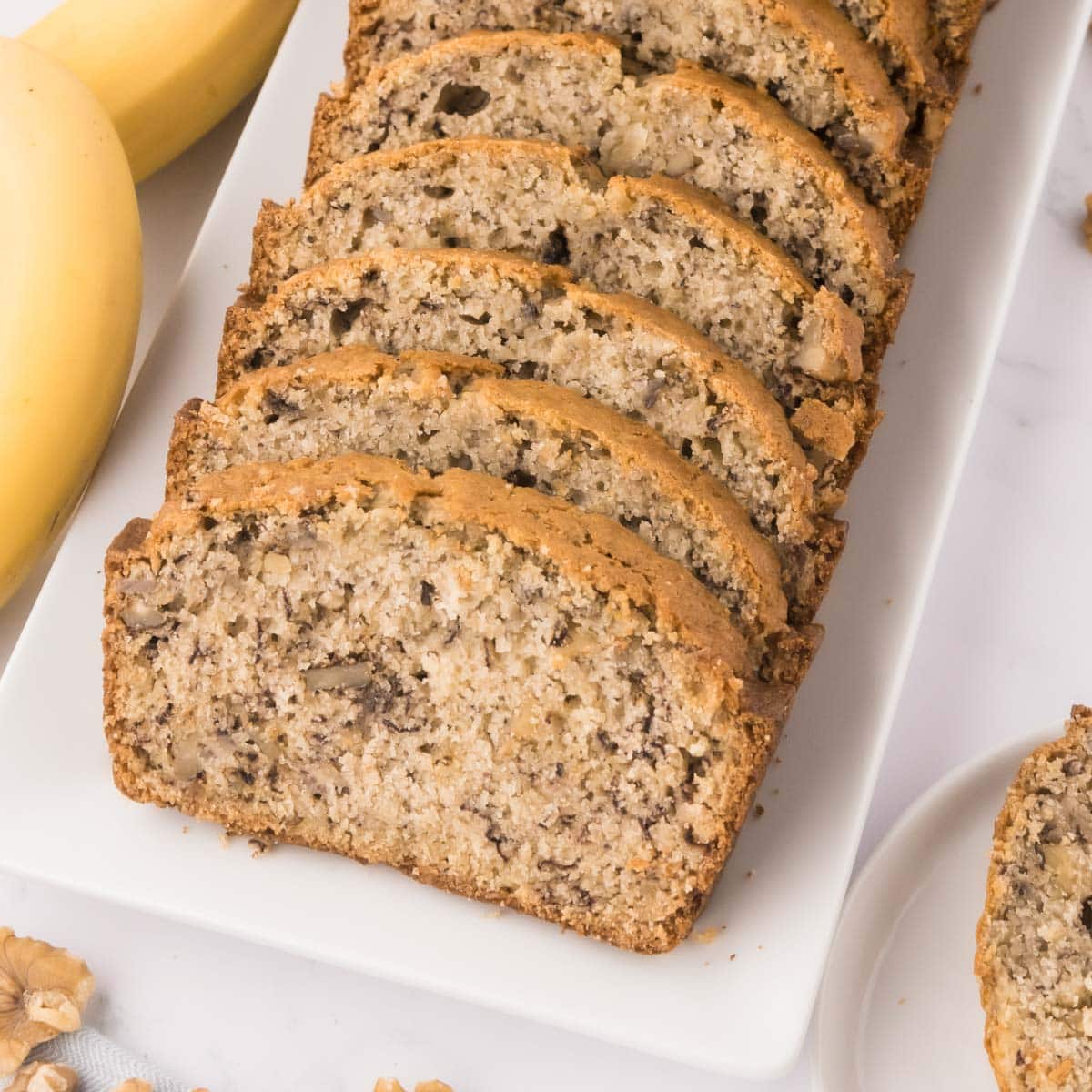 A white serving tray with sliced buttermilk banana bread with walnuts.